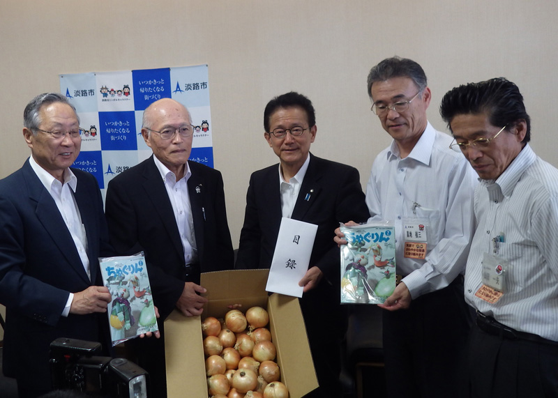 2015年6月のトピックス「「淡路島たまねぎ」と「ちゃぐりん」を贈る石田正組合長（左から2人目）と受け取る門康彦淡路市長（中央）」